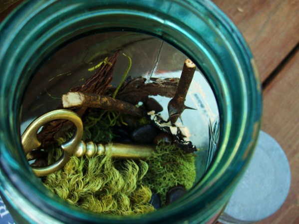 inside a mason jar terrarium with moss, forest finds, and an antique skeleton key