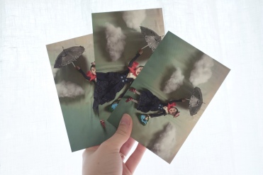 hand holding up three postcards featuring blue and red images of mary poppins