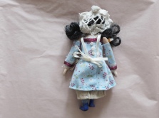 back of a miniature doll wearing period clothing, showing lace cap, apron, and tiny buttons